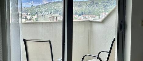 A balcony with two chairs, a view of a hilly landscape, and buildings in the distance.