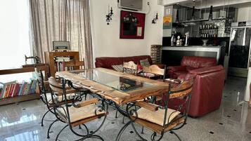 Un salón moderno con una mesa de comedor de vidrio, sofá de cuero y una zona de bar con estantes llenos de botellas.