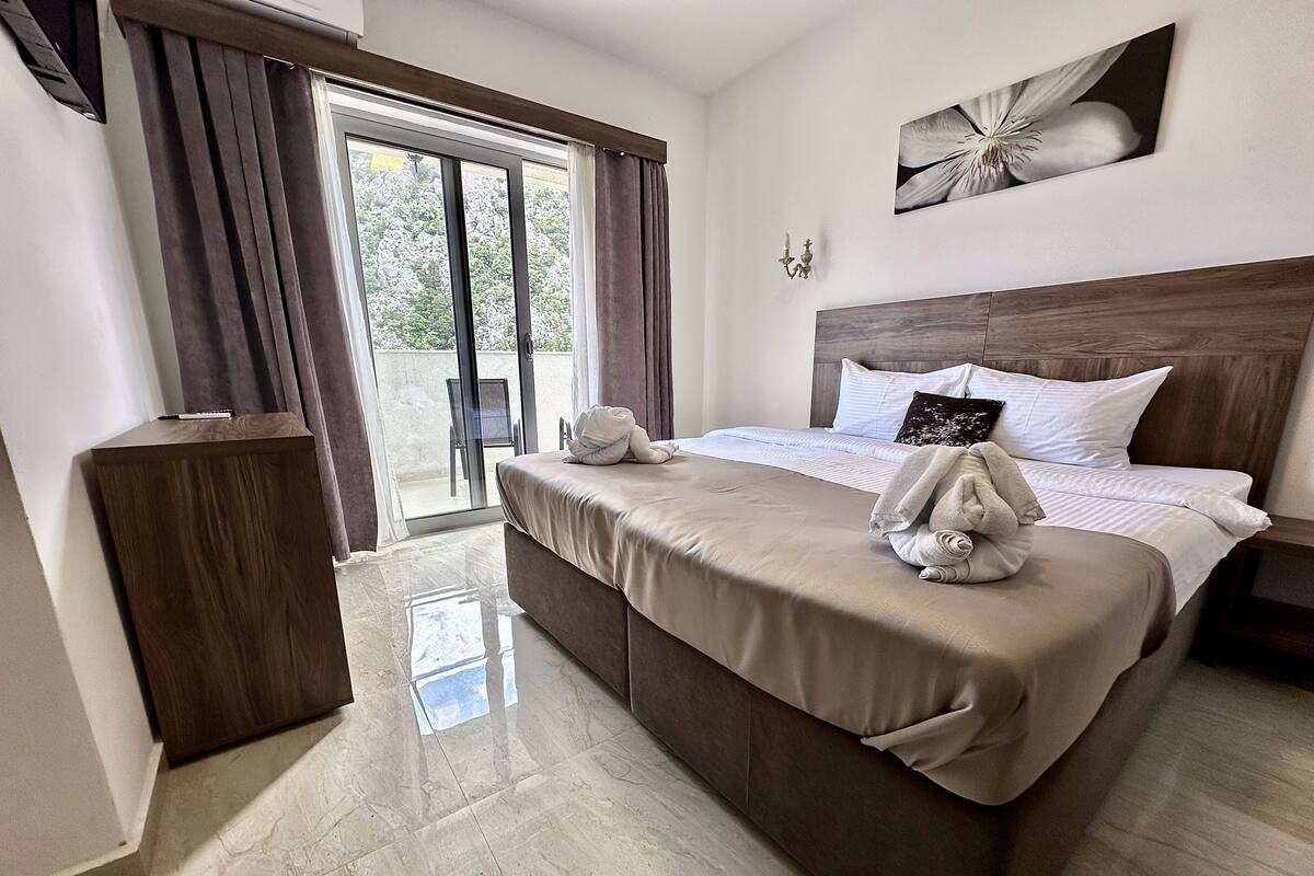 A hotel room with a bed, a wooden headboard, a painting, and a view through a glass door.