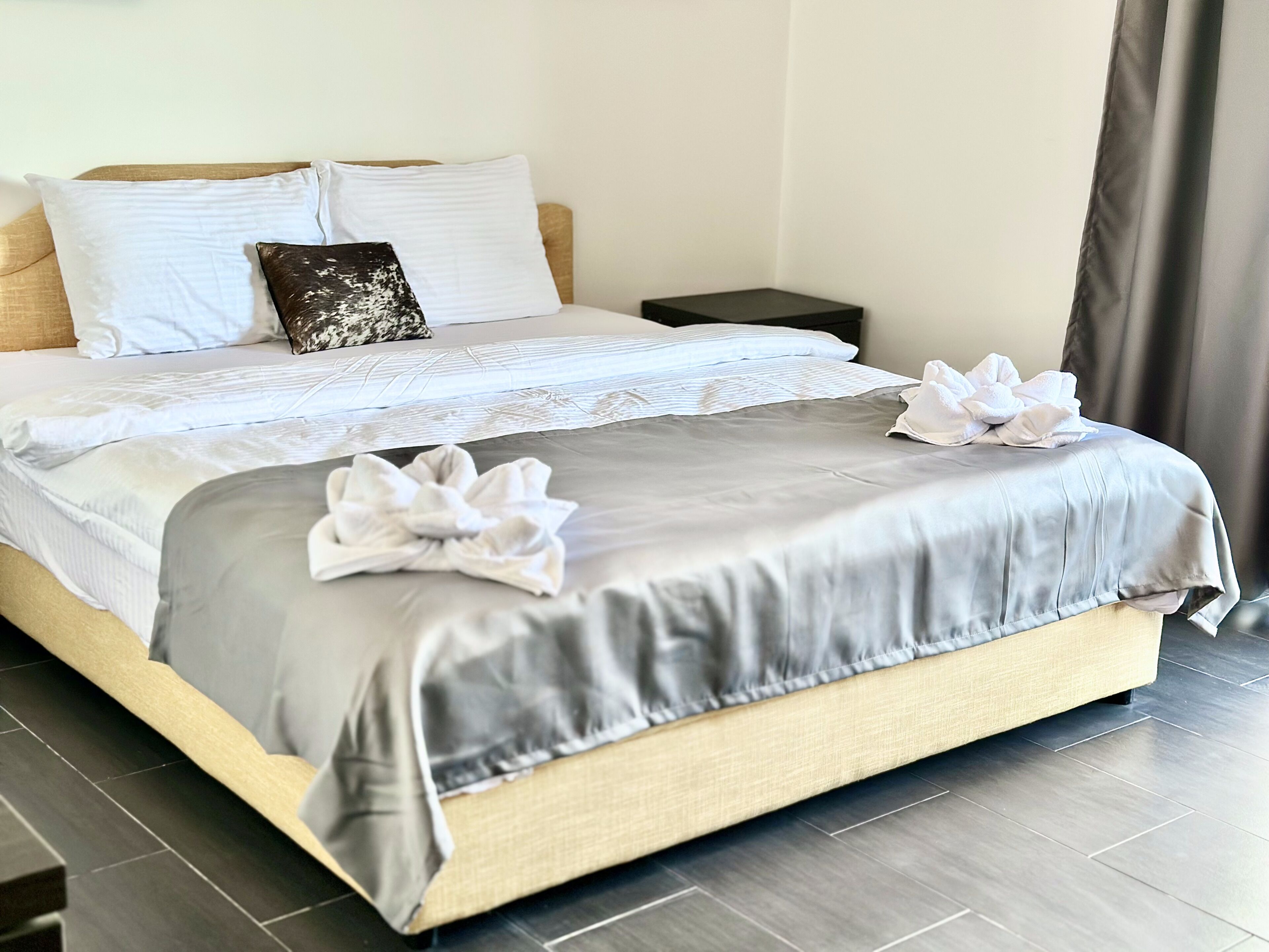 Een net opgemaakt bed met een grijs-witte dekbedovertrek, twee kussens en een decoratieve handdoek op het bed.
