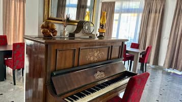 Un piano de cola en una habitación luminosa, con un espejo grande encima, un reloj y objetos decorativos en la repisa de la chimenea.