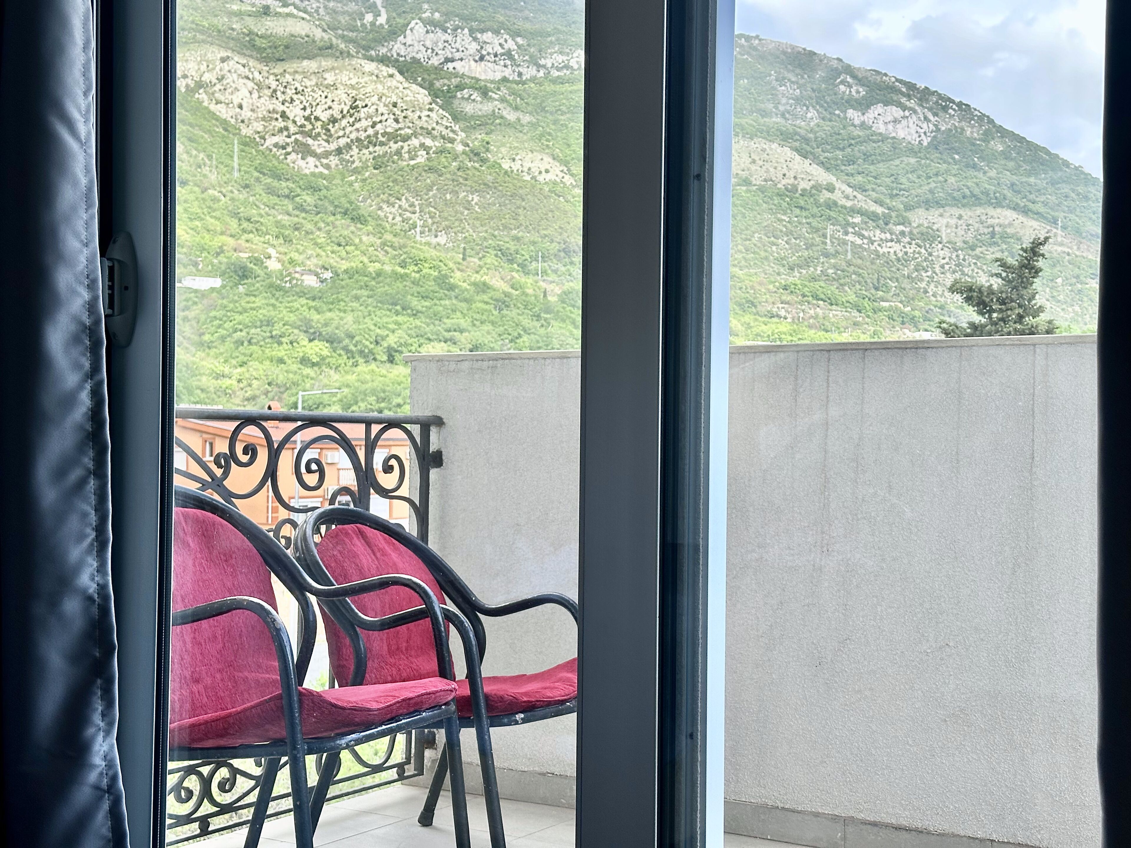 A balcony with a metal railing and red cushioned chairs, overlooking a mountainous landscape.