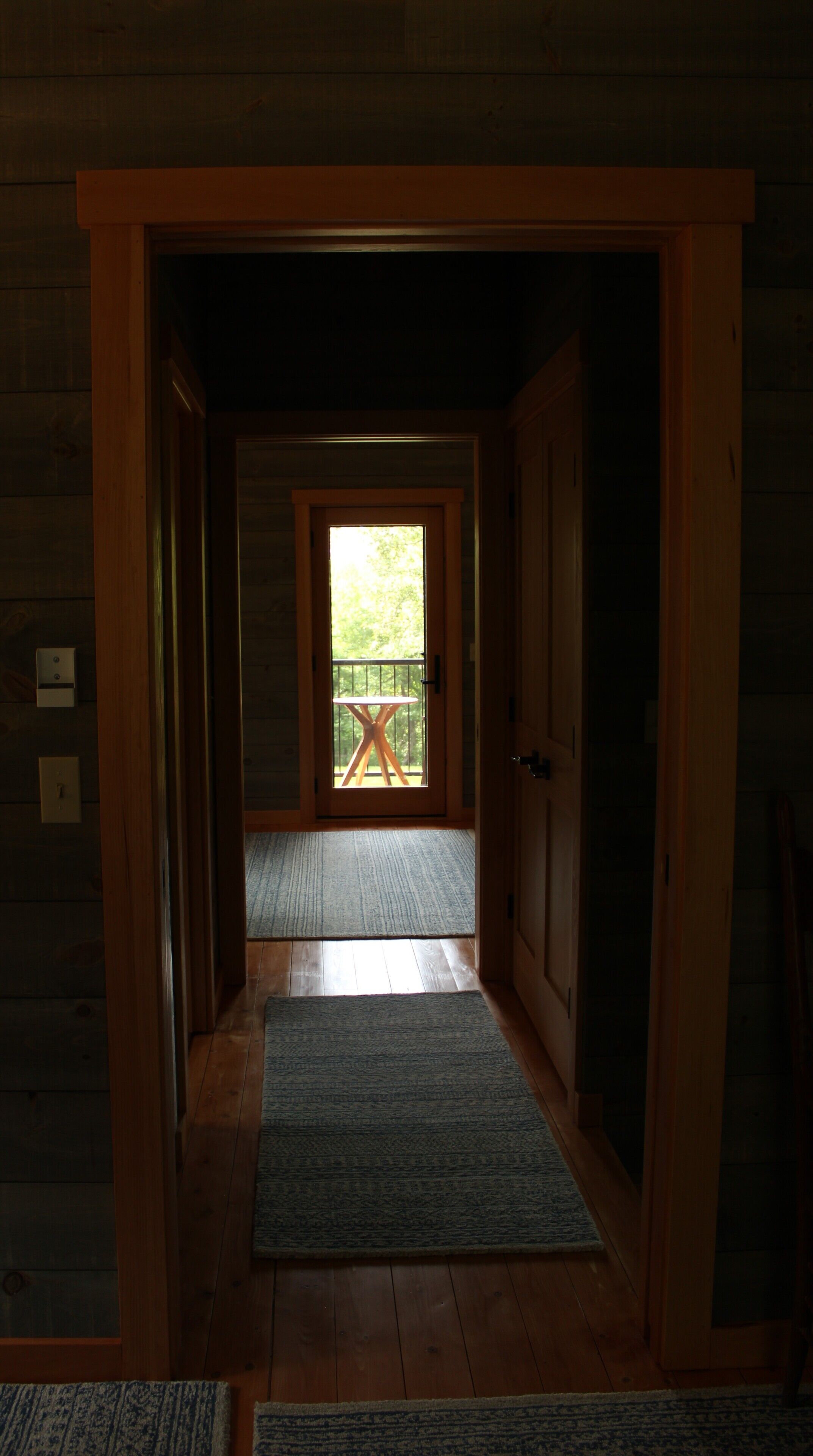 A wooden interior hallway leading to a balcony with a table and chairs.