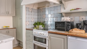 Een keuken met een kookplaat, oven, magnetron en koffiezetapparaat. Er zijn kastjes, een aanrecht en een schaal met fruit.