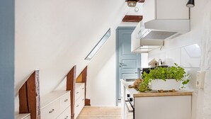 Cocina estrecha con escalones de madera, un armario blanco, una puerta azul y una encimera con productos frescos.