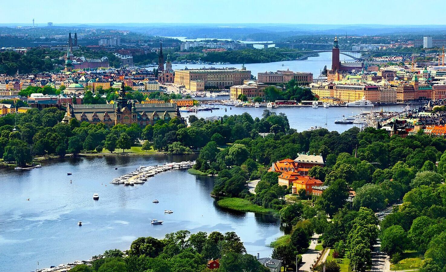 A riverside cityscape with historic buildings, a bridge, and a park with boats.
