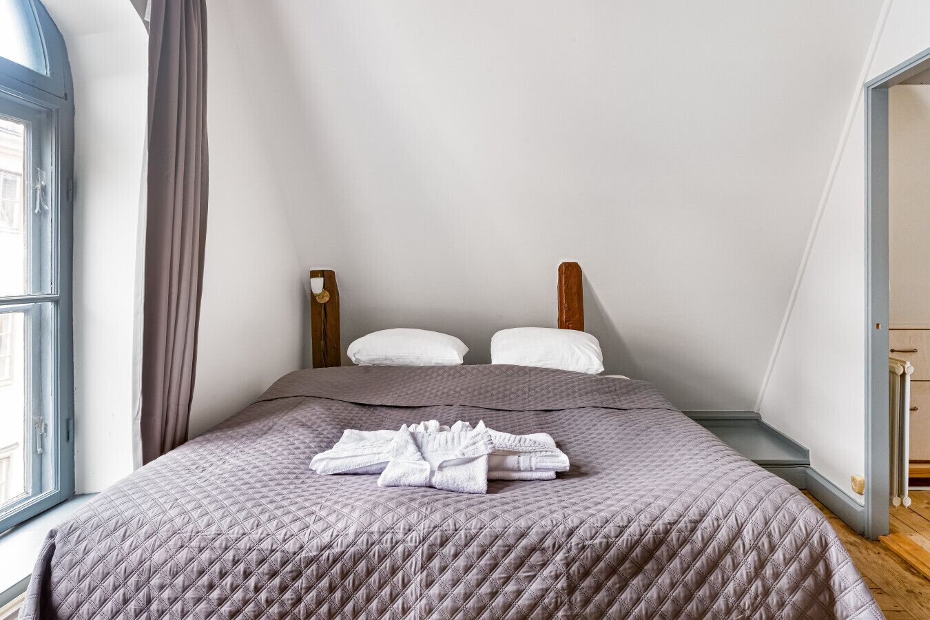 A bedroom with a bed, pillows, a window, and a curtain.