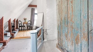 Una escalera estrecha con barandal de madera, una puerta rústica y una pequeña mesa con sillas al fondo.