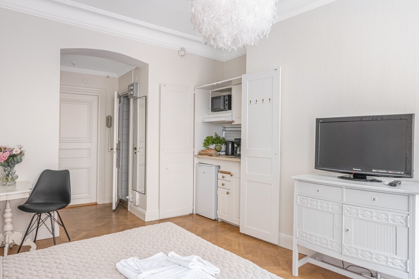 Une pièce moderne et bien éclairée, dotée d’un téléviseur à écran plat, d’une table à manger avec des chaises, d’un coin cuisine avec des placards et d’un élégant luminaire décoratif au plafond.