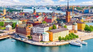 A panoramic view of a city with historic buildings, a prominent church tower, and a river with boats. - Unik lägenhet i gamla stan (Södermalm)