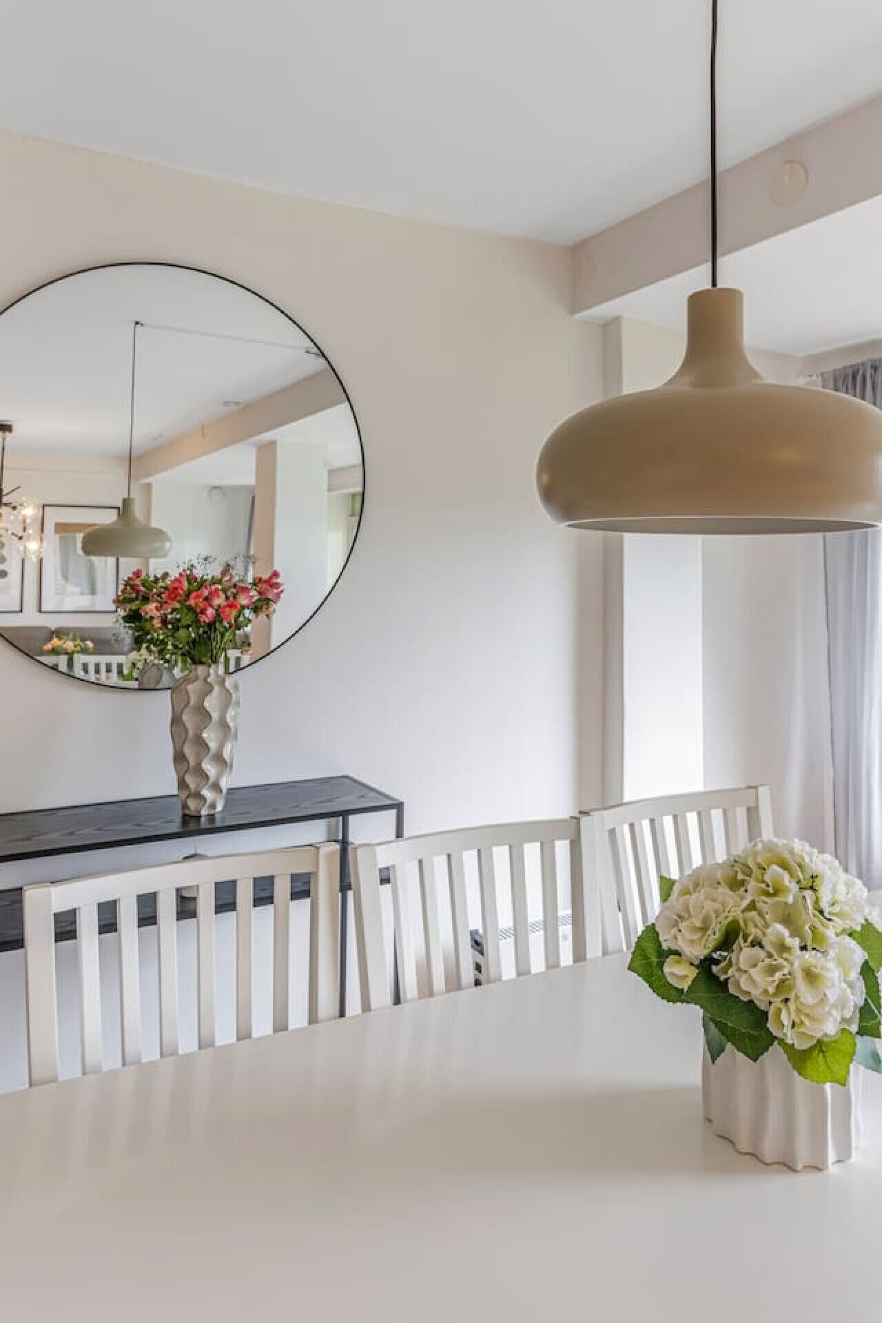 A dining area with a white table, a round mirror, and two hanging pendant lights.