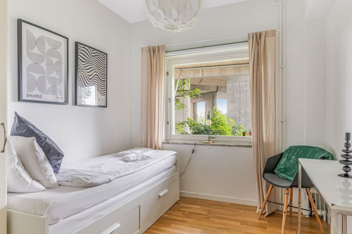 Ett litet, modernt rum med en säng, ett skrivbord och ett fönster med utsikt över grönområden.
