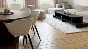 Un salon moderne avec une table de salle à manger ronde en bois, des chaises blanches, un canapé beige et une table basse noire.