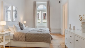 Une chambre bien rangée, avec un lit, des tables de chevet, une commode et une fenêtre avec des rideaux.