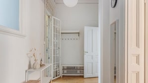 Un couloir avec un plancher en bois, des murs blancs, un banc, une porte blanche et une étagère blanche sur laquelle se trouve un vase.