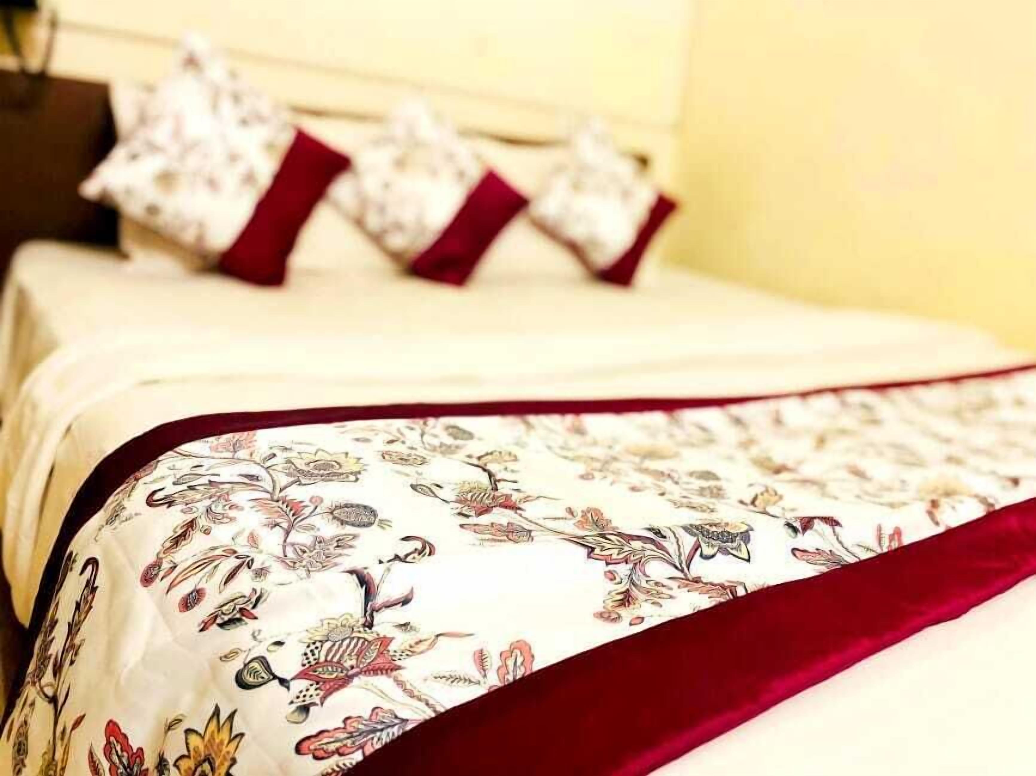 Una cama con colcha estampada de flores y almohadas rojas.