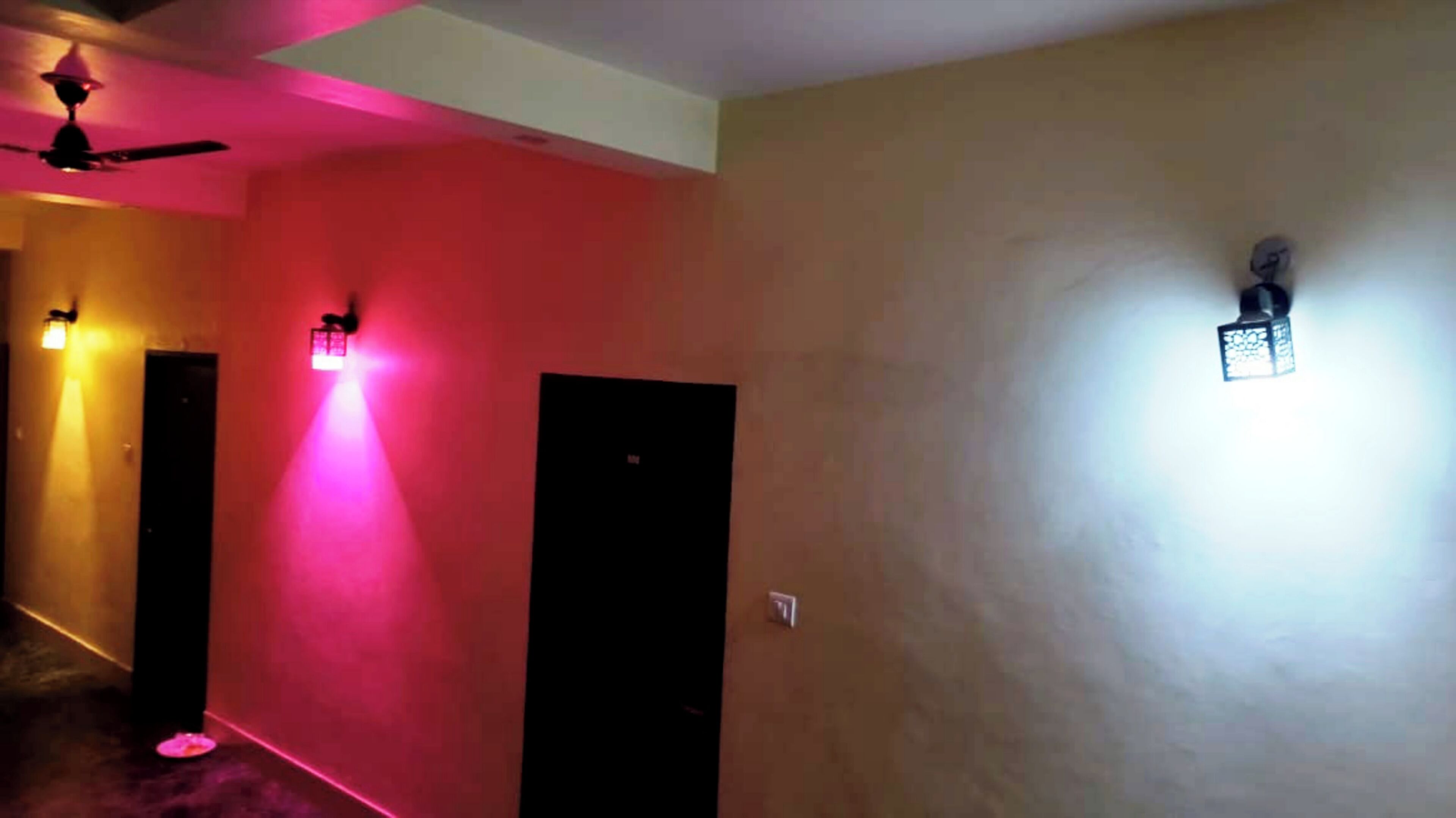 Um corredor com ventoinha no teto, uma porta com luminária e uma luminária fixada na parede.