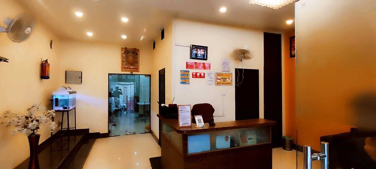 Zona de recepción de hotel con mostrador, pantalla digital y mampara de vidrio.