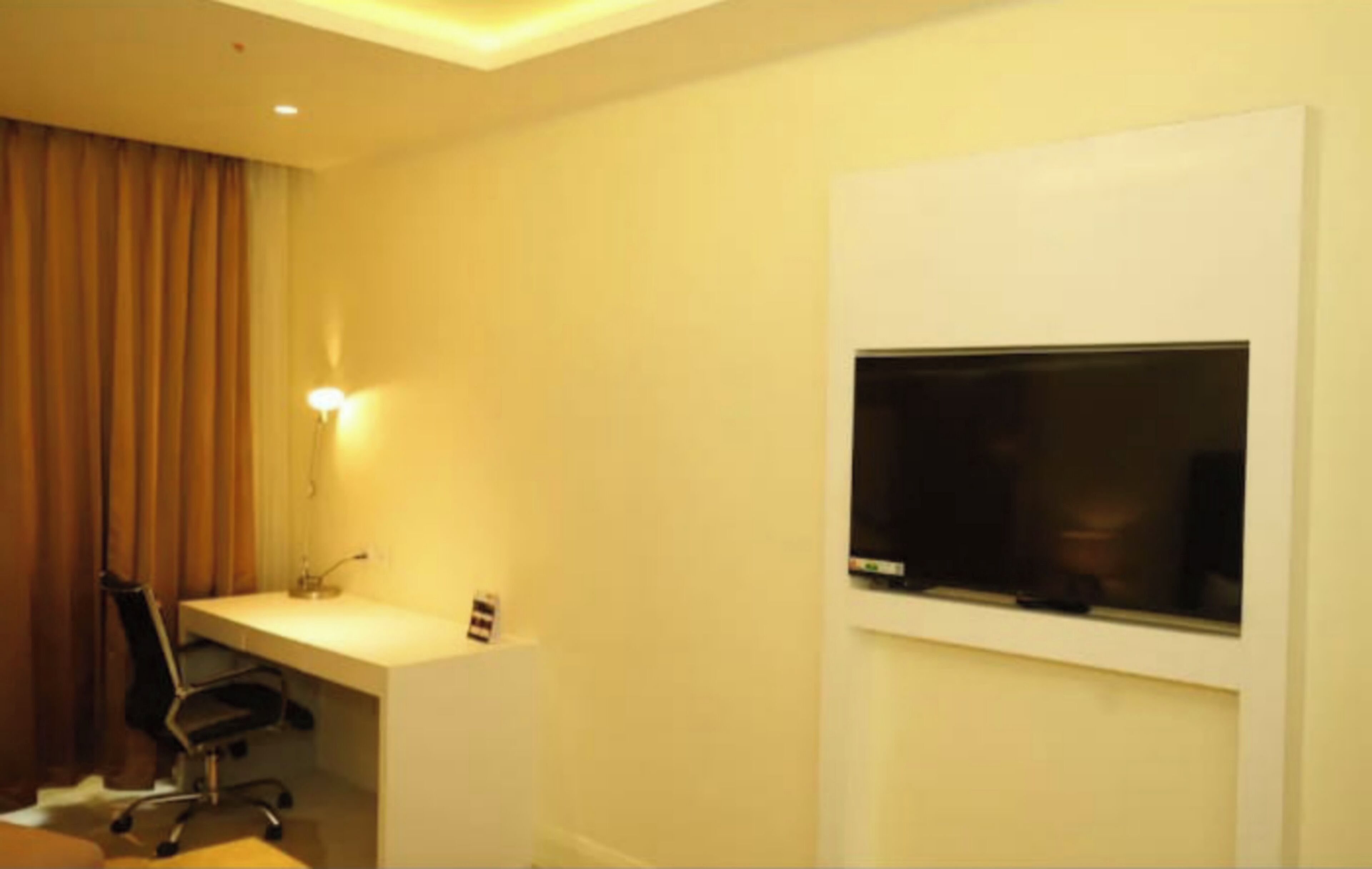 Una camera d'albergo con una scrivania, una sedia e una televisione fissata al muro.