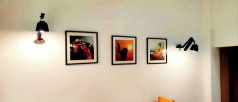 A hotel room with a bed, two pillows, a nightstand, a lamp, and three framed pictures on the wall.