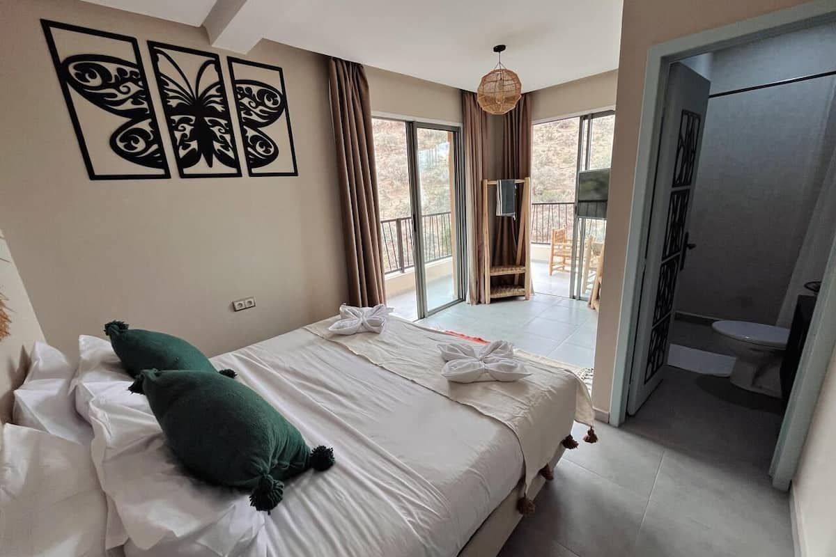 A bedroom with a bed, pillows, a balcony, and a bathroom.