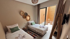 A hotel room with two beds, a small side table, and a view of the outdoor area. - Harmony surf lodge (Imi Ouaddar)