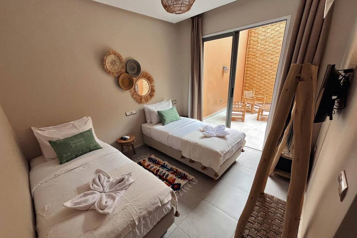A hotel room with two beds, a small side table, and a view of the outdoor area.