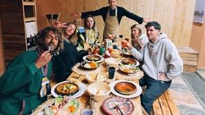 A group of people around a wooden table with various dishes, suggesting a communal dining setting. - Harmony surf lodge (Imi Ouaddar)
