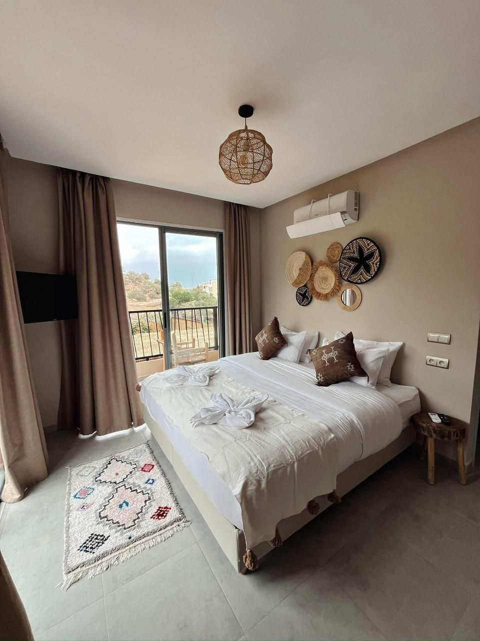 A spacious bedroom with a large bed, a balcony view, a television, and decorative wall art.