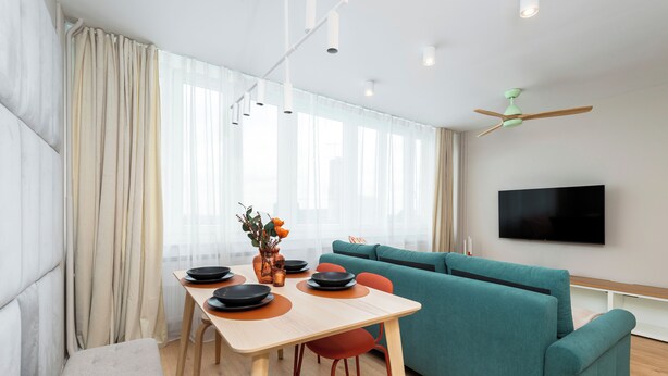 Un saló modern amb un sofà color aquamarina, una taula de dinar amb caires i un televisió plana penjada a la paret.