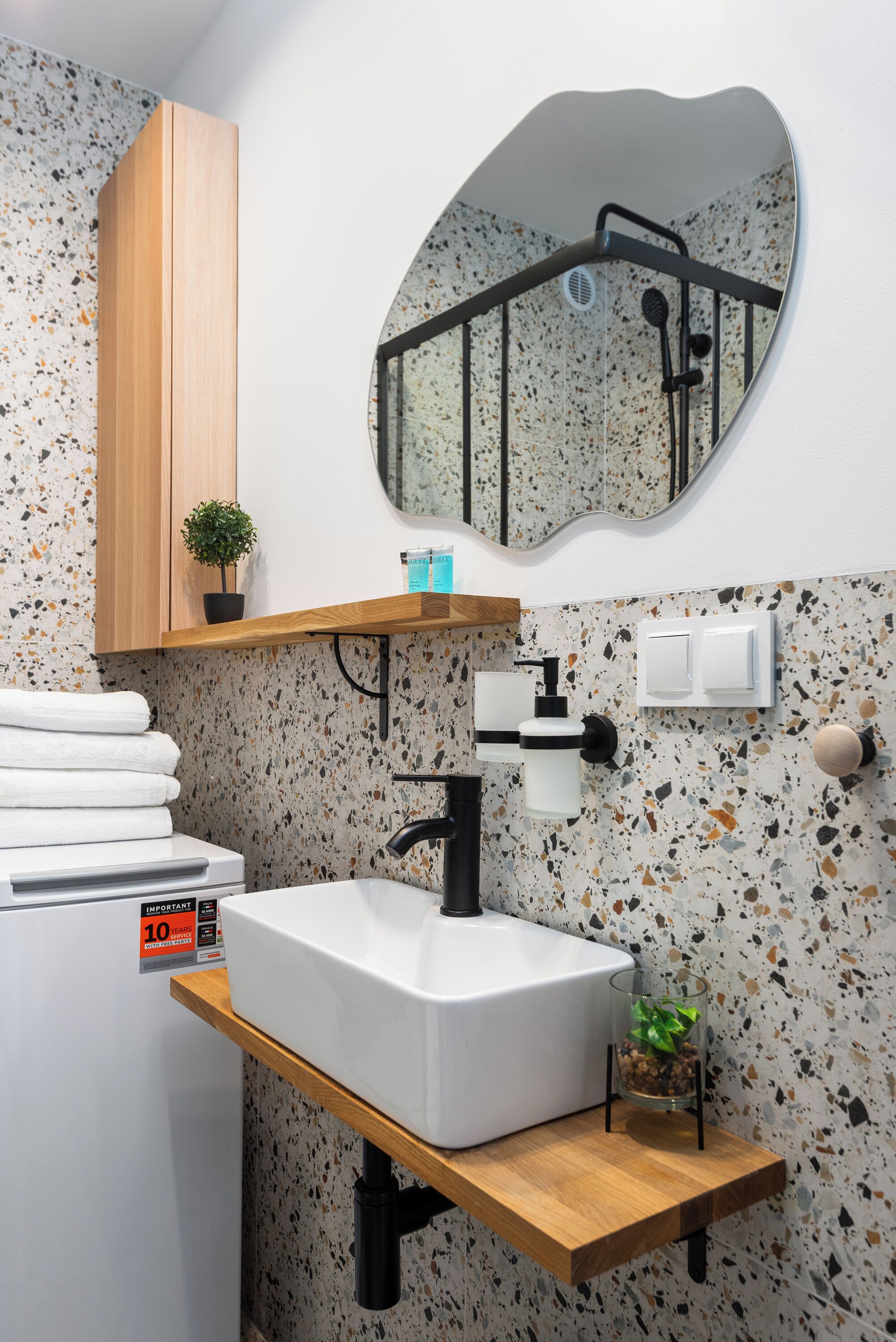 Une salle de bain avec un lavabo blanc, un meuble en bois, un miroir et un pare-éclaboussures à motifs.
