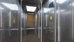 Un ascensor modern amb parets d'acer inoxidable, barana i panell de control amb botons.