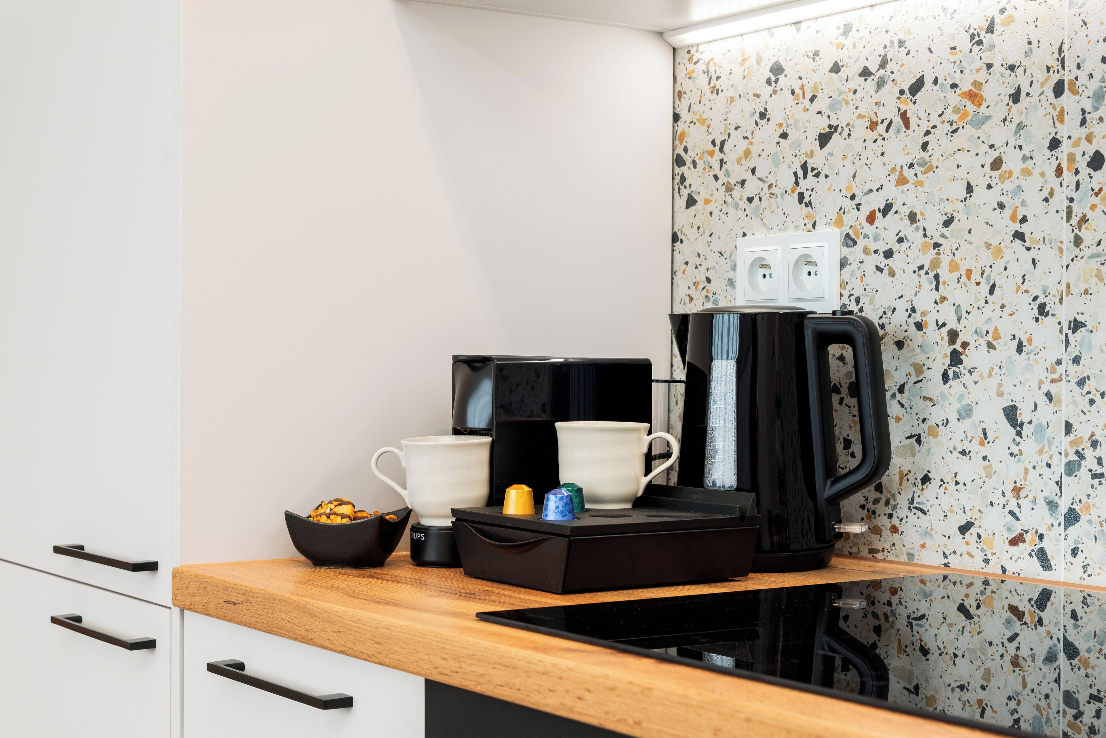 Une cuisine avec un plan de travail, une machine à café, deux tasses blanches, un bol et un petit récipient bleu.