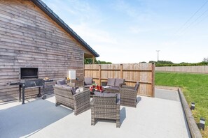 En udendørs terrasse med grill, fletmøbler og et træhegn.