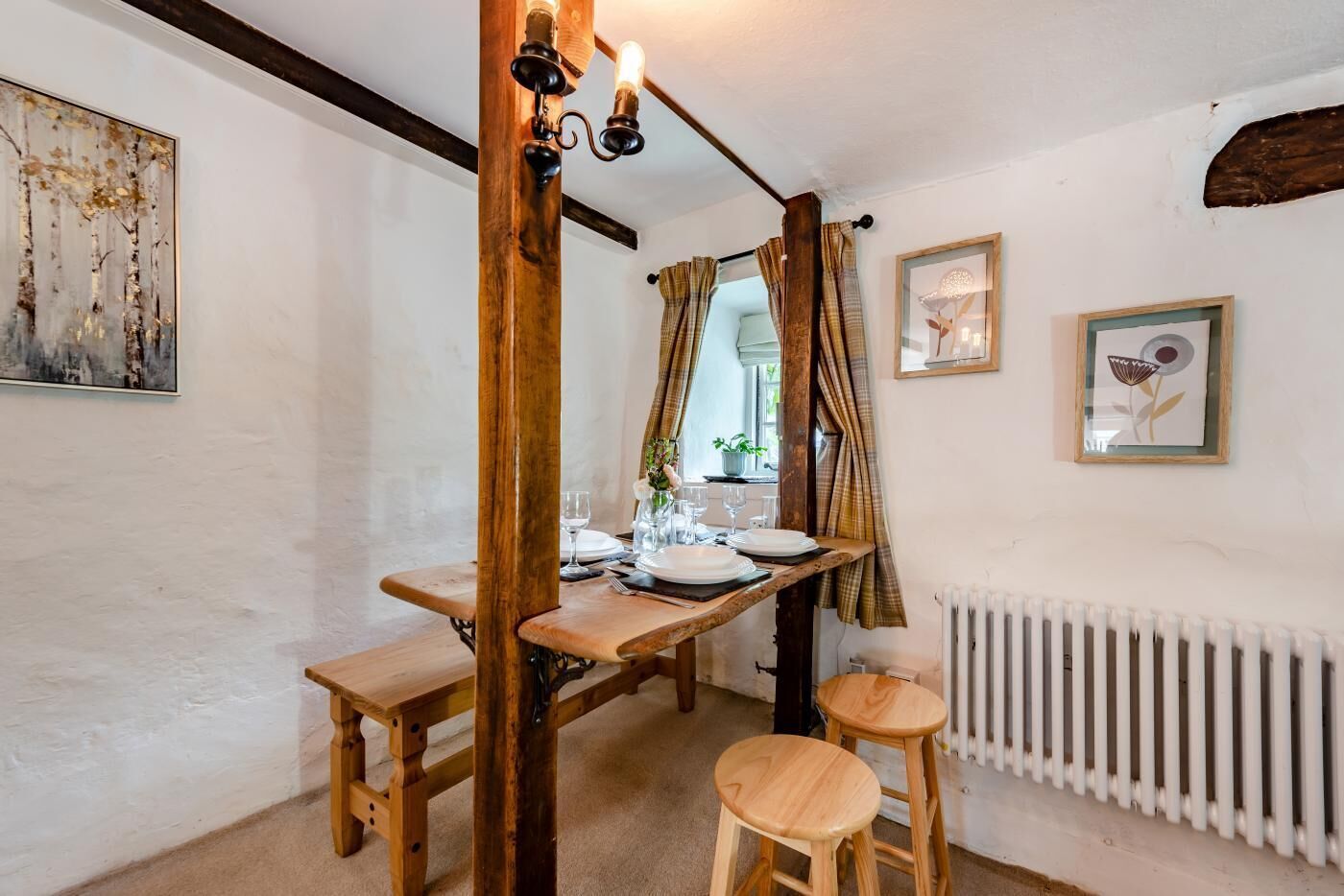 A dining area with a wooden table set for two, a rustic chandelier, and a radiator.