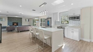 Een moderne keuken met witte kasten, een groot eiland met barstoelen, een inbouwoven en een accentmuur van steen.