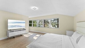 Een slaapkamer met een bed, een televisie, een raam met uitzicht op bomen en een plafondlamp.