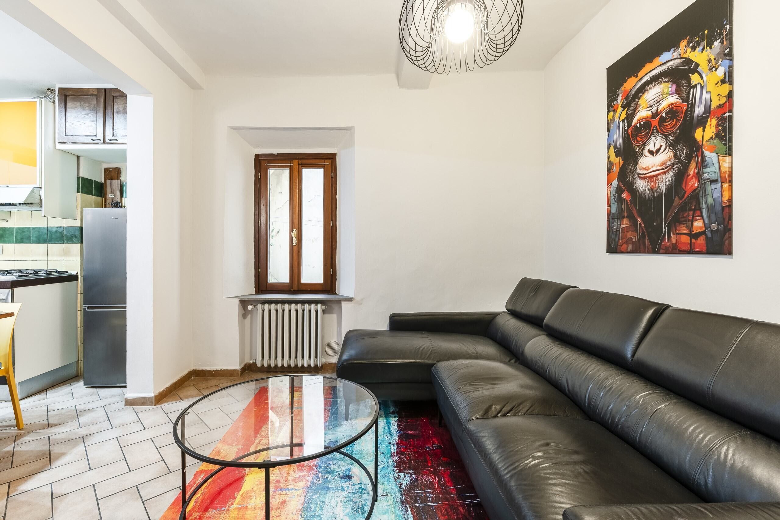 Un saló amb un sofà de cuir negre, una taula de centre de vidre i una catifa colorida.