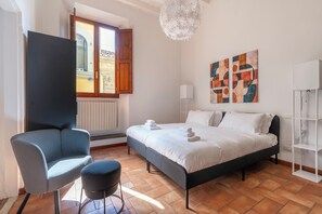 A bedroom with a bed, a chair, a small table, a radiator, a window, and a chandelier. - Vigna Nuova First Floor (Firenze)