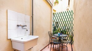 Un pequeño patio al aire libre con un lavamanos blanco, un cerramiento de celosía verde y una mesa redonda con sillas.