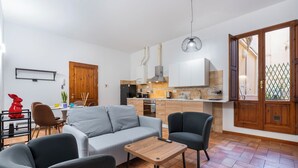 Una sala de estar moderna con sofá, sillas, una mesa de centro y una zona de cocina con armarios y electrodomésticos.