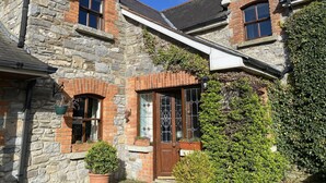 Un bâtiment en pierre et en briques, de conception traditionnelle, avec une entrée centrale dotée d’une porte et de fenêtres, le tout agrémenté de plantes en pot et d’un petit jardin.