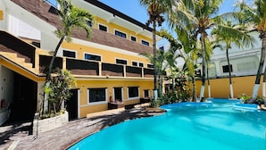 Un hôtel doté d’une piscine entourée de palmiers et d’un immeuble à plusieurs étages avec des balcons.