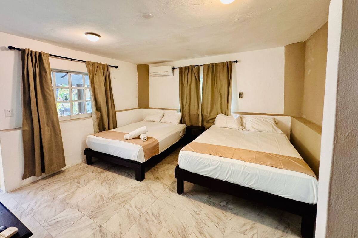 Une chambre d’hôtel avec deux lits, une fenêtre avec des rideaux, un appareil de climatisation et un sol carrelé.
