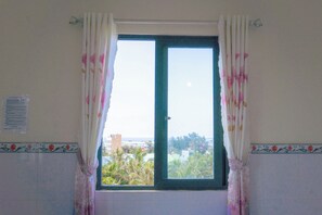 Una habitación con ventana, cortinas, un muro con azulejos y vistas a edificios y árboles.