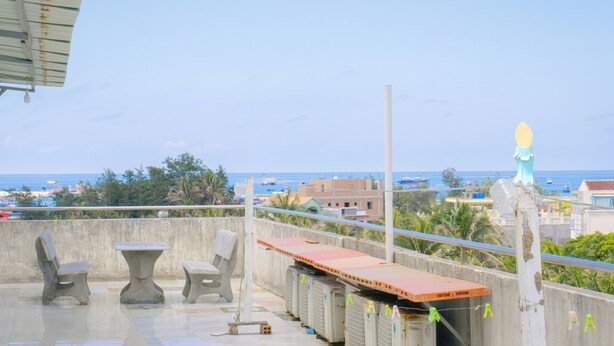 Une terrasse sur le toit, avec des meubles en béton, une vue sur la mer et des bâtiments en arrière-plan.