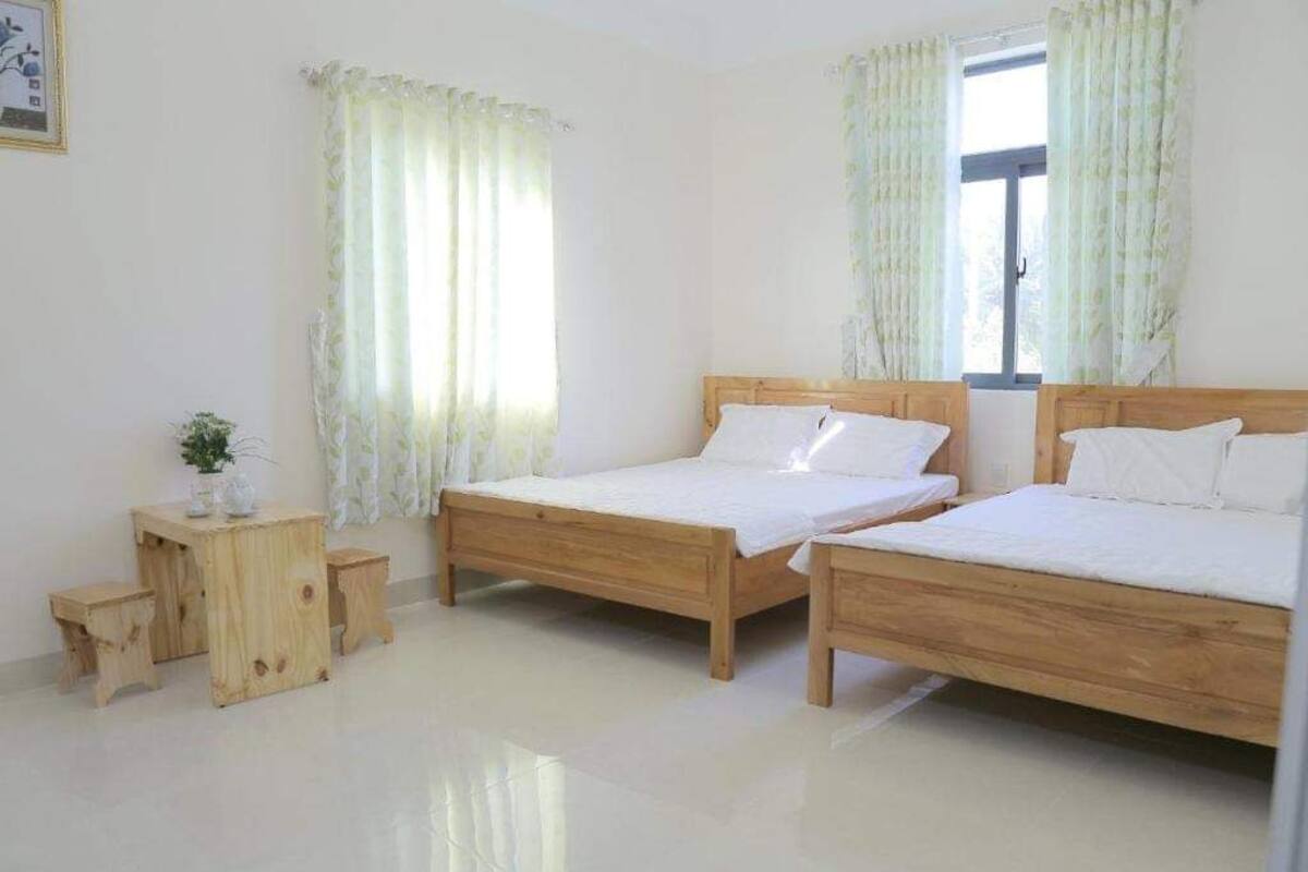 A room with two wooden beds, a small wooden table, and a window with curtains.
