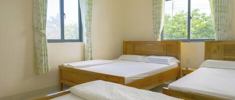 A room with two wooden beds, a window with curtains, and a view of greenery outside.