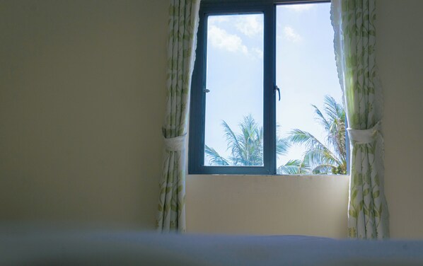 A room with a window, curtains, and a view of palm trees.