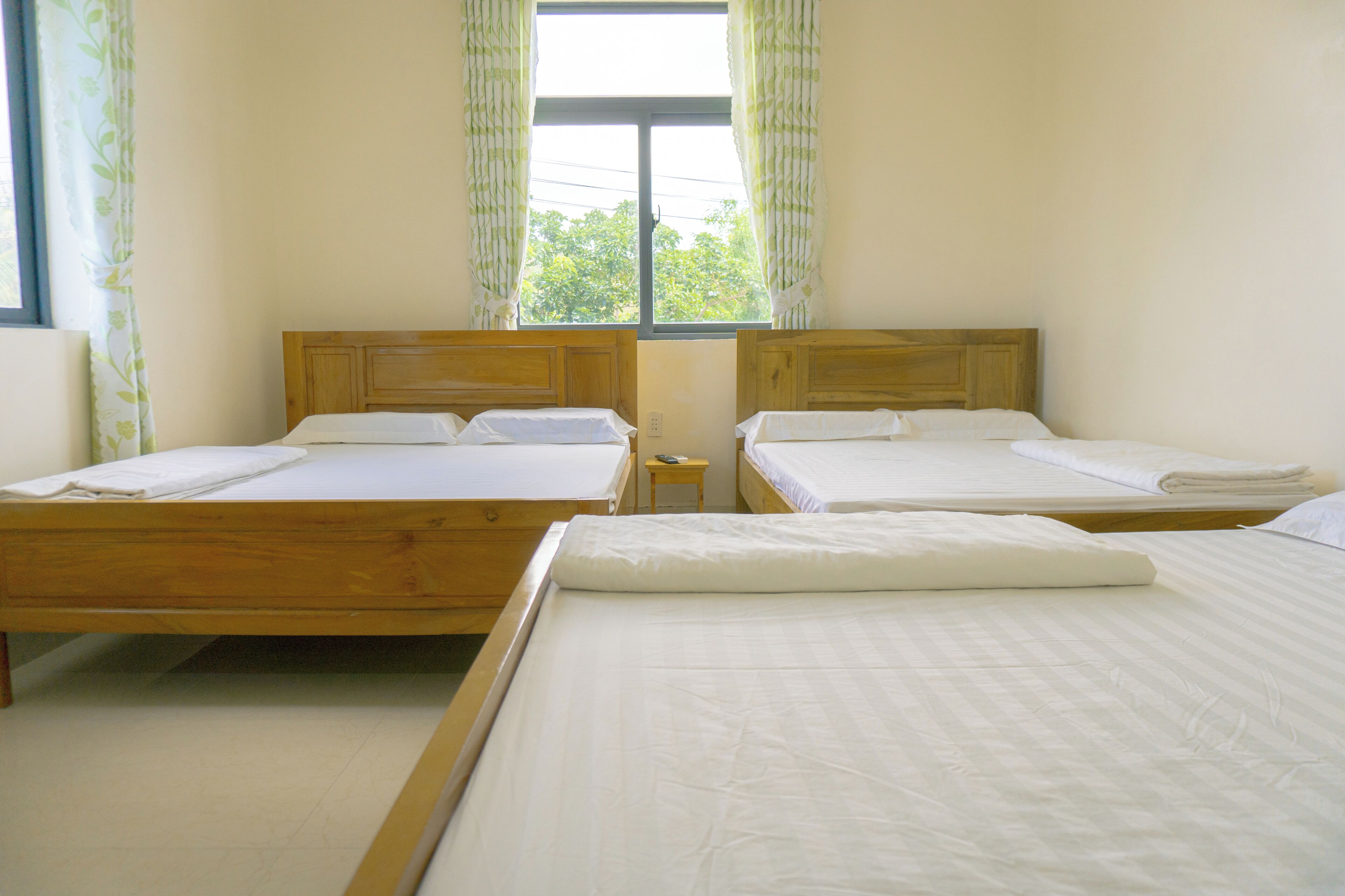 A room with two wooden beds, a small table, and a window with curtains.